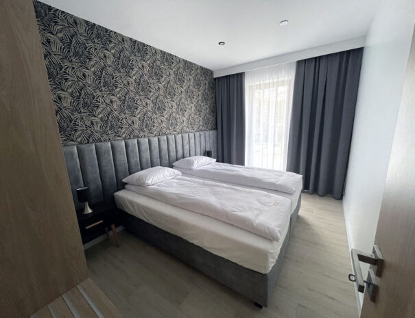 Elegancka sypialnia apartamentu wakacyjnego PATIO w Łagowie — tapeta z motywem botanicznym, wygodne łóżka, stonowany wystrój