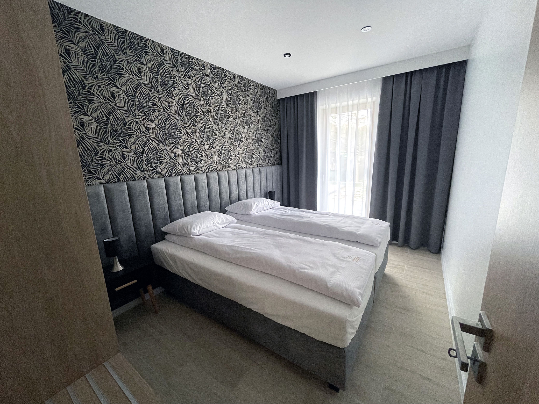 Elegancka sypialnia apartamentu wakacyjnego PATIO w Łagowie — tapeta z motywem botanicznym, wygodne łóżka, stonowany wystrój